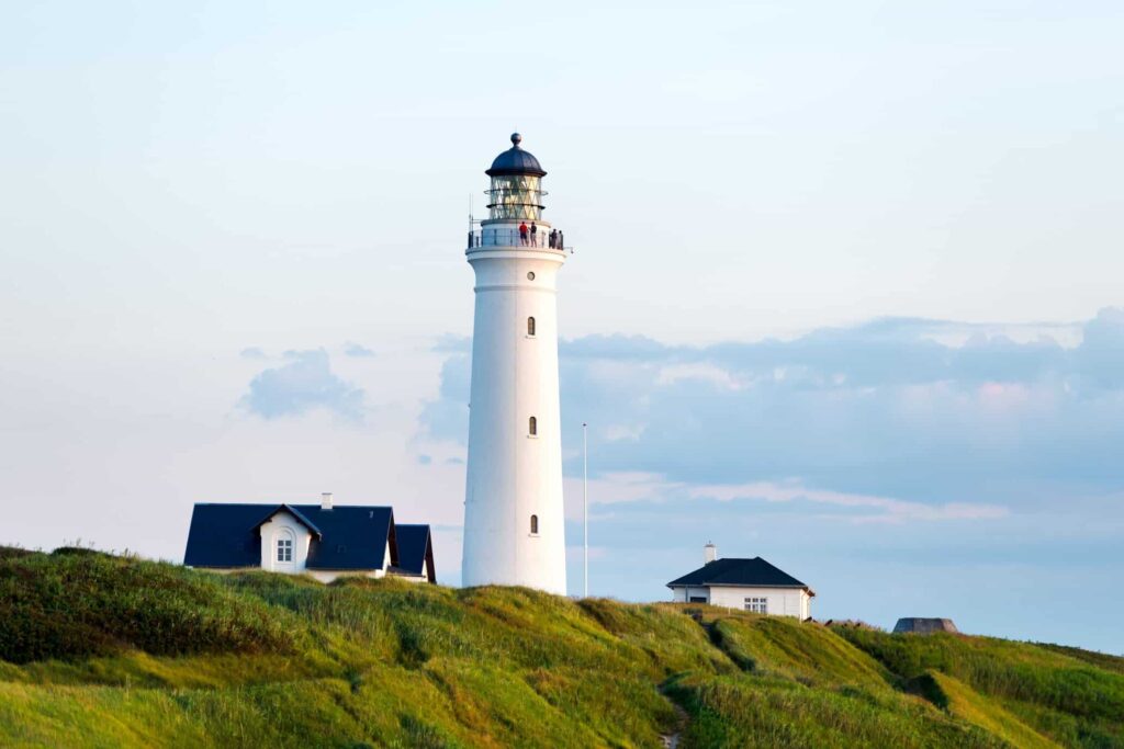 Et hvidt fyrtårn med 2 hvide huse med sort tag i Hirtshals