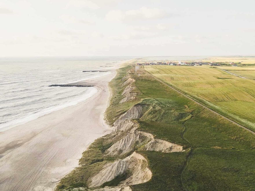 Nogle klitter ved havet, hvor der er græsmarker bag klitterne.